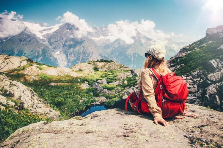 dziewczyna z plecakiem siedzi w górach i podziwia krajobraz, leć do skandynawii