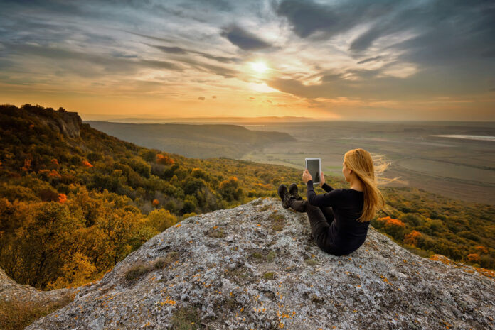kobieta robi zdjęcia tabletem na szczycie skały
