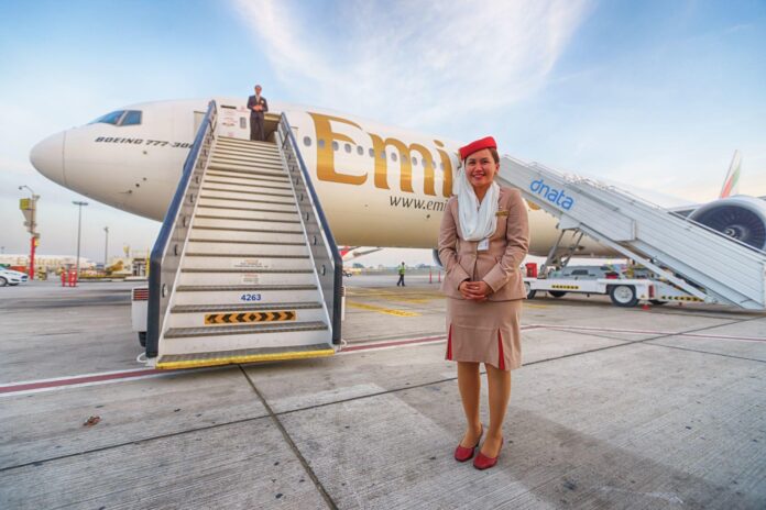 Stewardesa stojąca na lotnisku przed samolotem linii Emirates