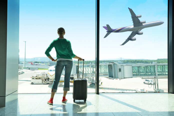 kobieta czeka na lotnisku z bagażem patrząc na samolot