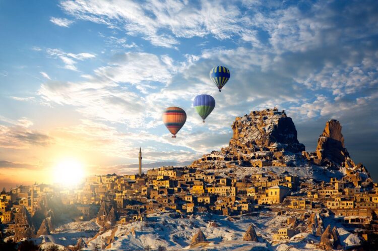 trzy kolorowe balony na niebie podczas wschodu słońcu lecące nad doliną z budowlami wykutymi w skale