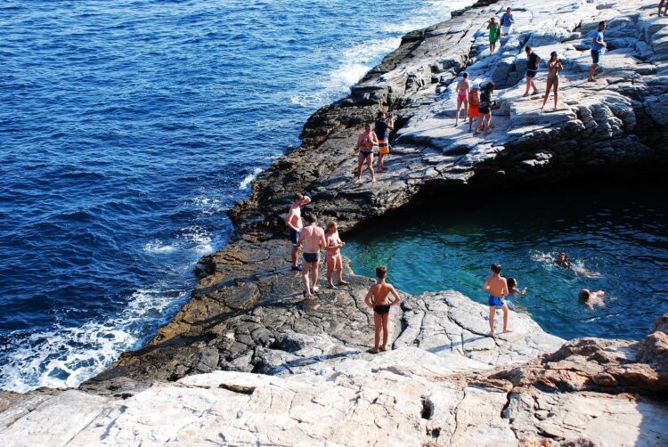turyści w strojach kąpielowych na skałach przy naturalnym basenie na tle morza