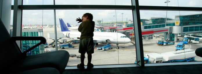Dziecko oparte o szybę w terminalu patrzy na płytę lotniska