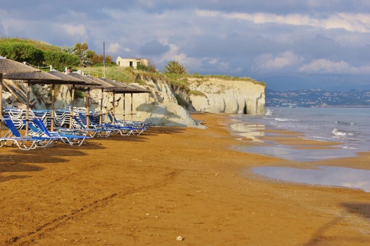 plaża z czerwonym piaskiem otoczona klifami z leżakami i parasolami ze słomy