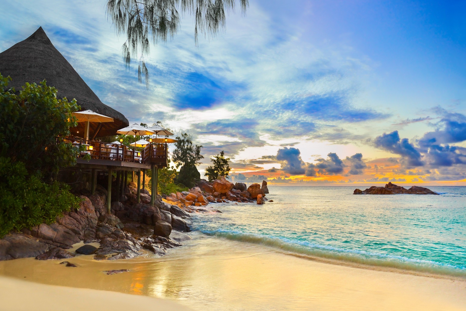 restauracja na plaży otoczona zielenią postawiona na palach z widokiem na lazurowe morze i błękitne niebo