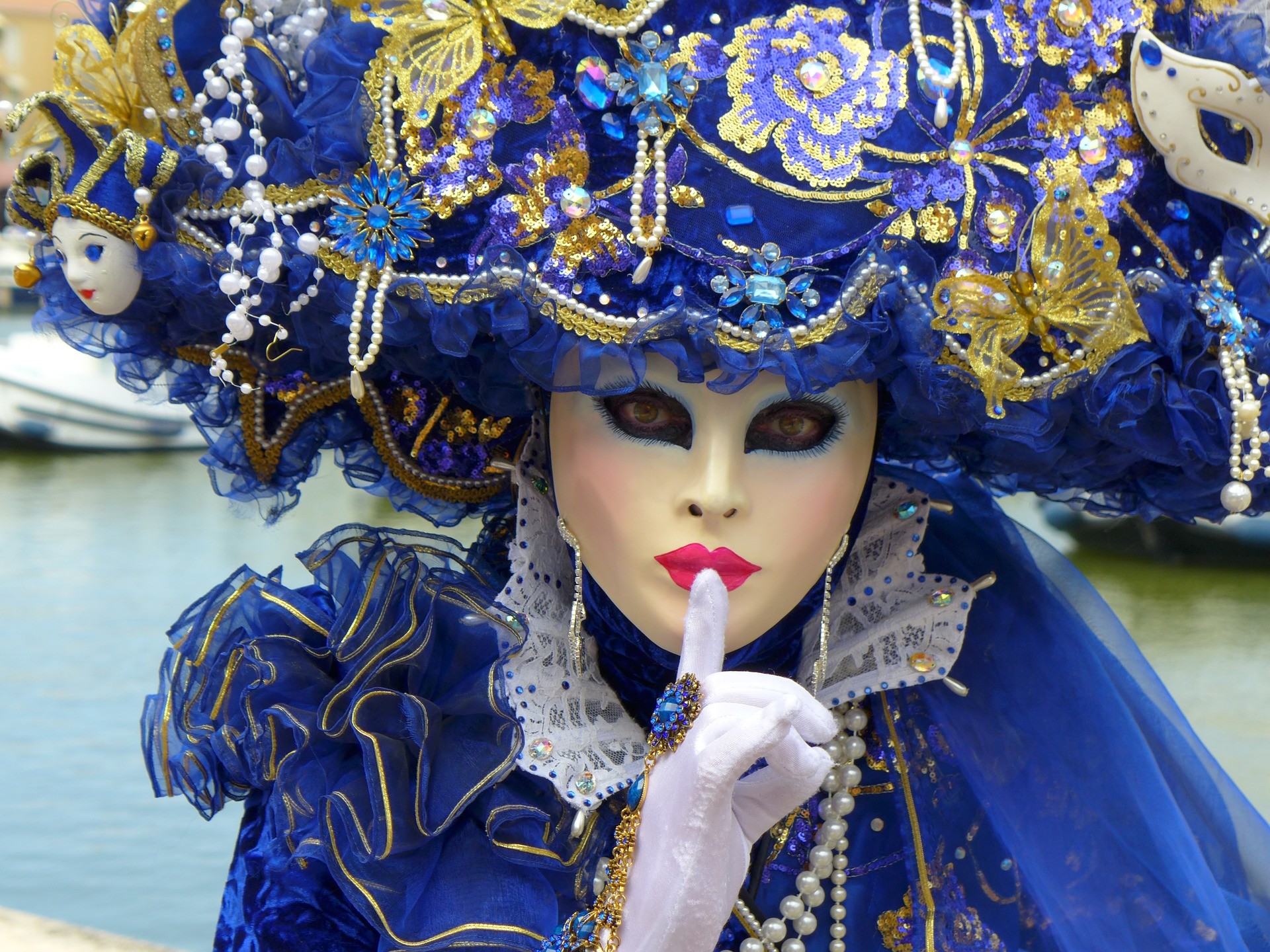 kobieta w niebieskim stroju karnawałowym ze zdobieniami i weneckiej masce przykładająca palec do ust
