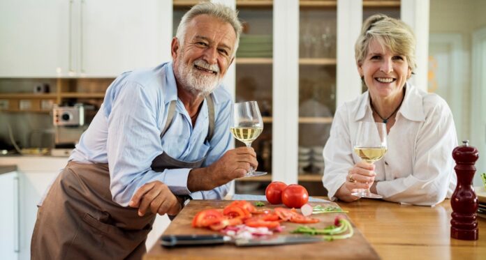 mężczyzna i kobieta trzymający kieliszki z białym winem w kuchni na tle białego regału