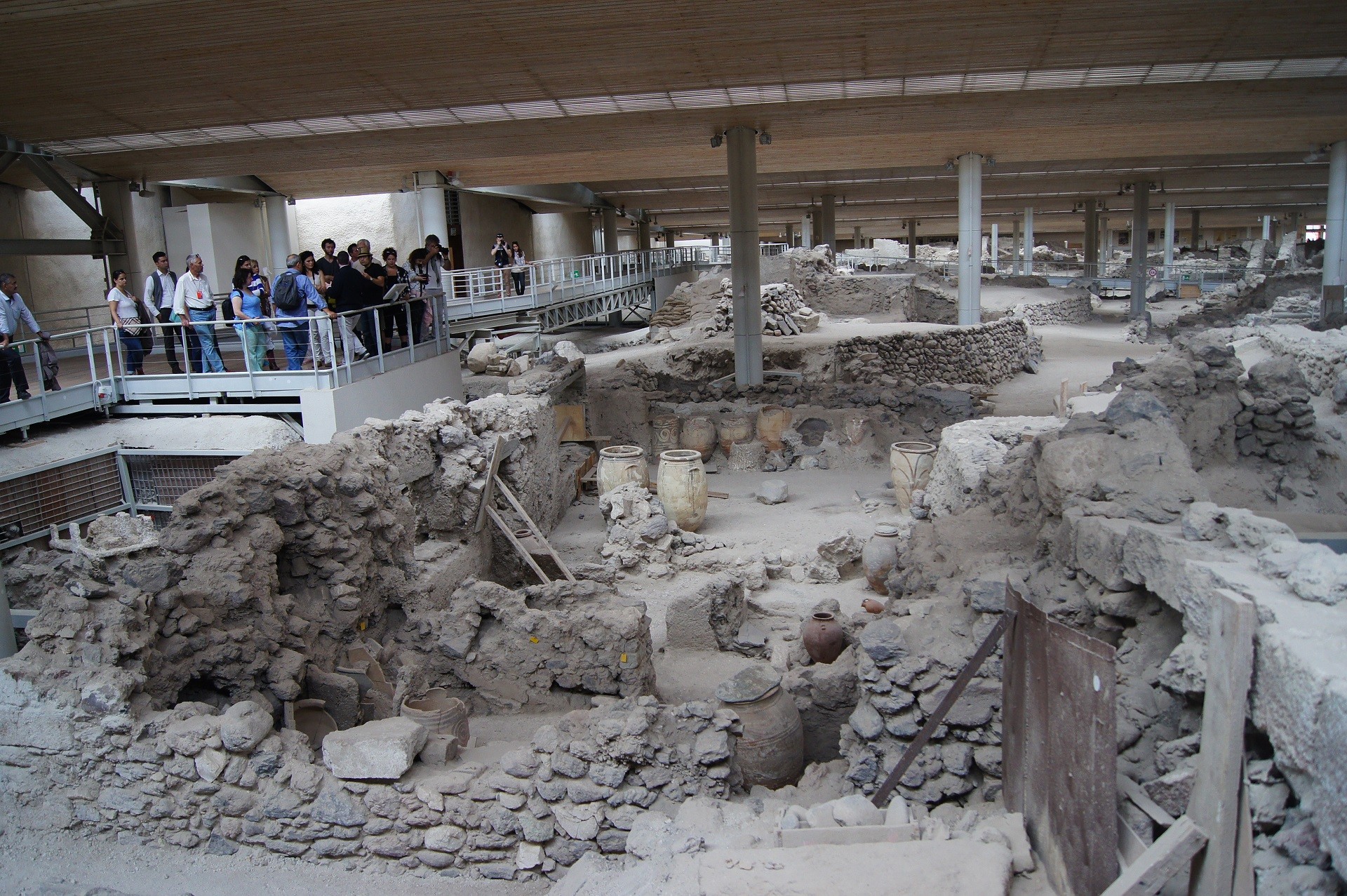 turyści oglądający stanowisko archeologiczne z ruinami kamiennych domów z wazami ceramicznymi