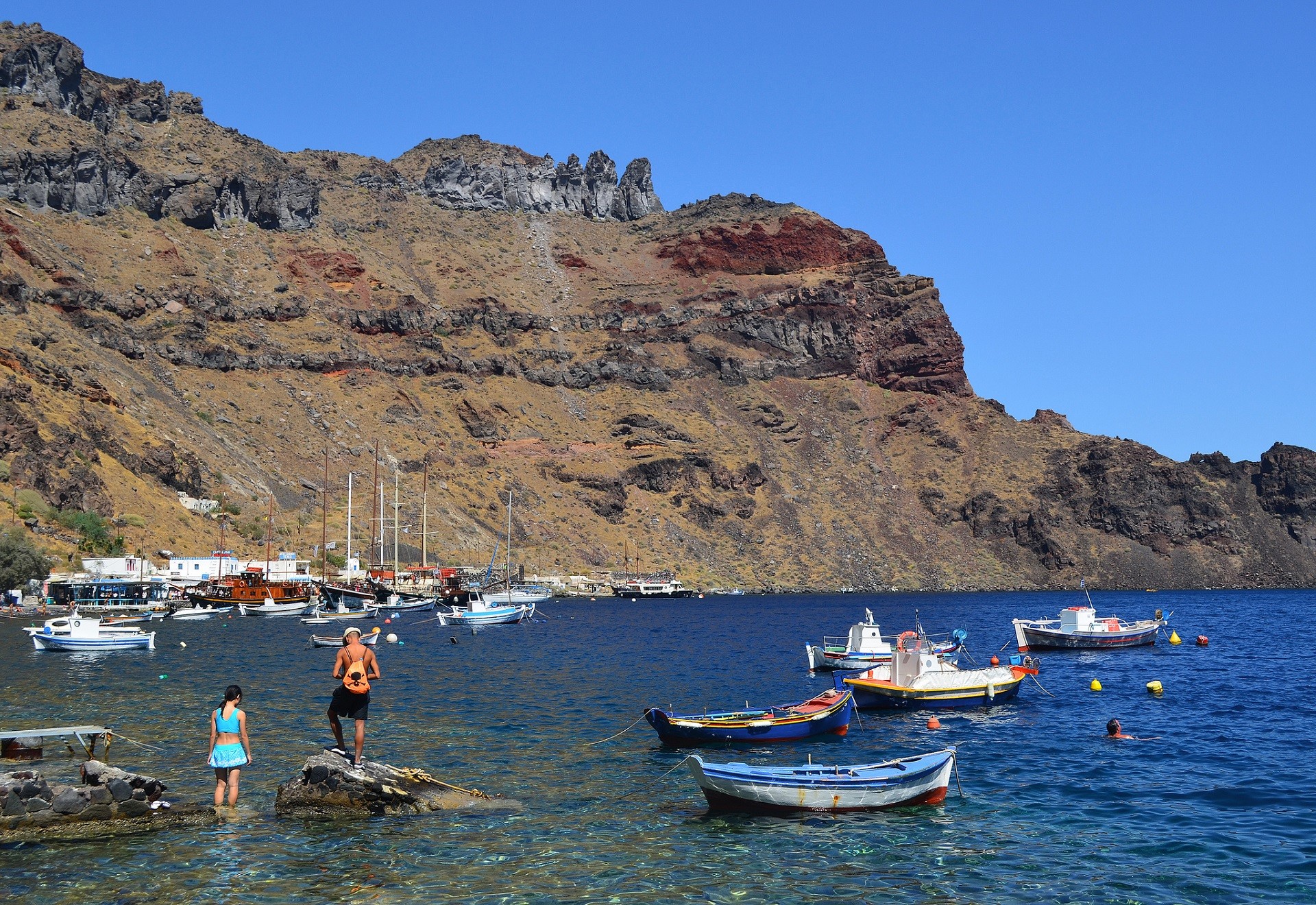 kolorowe łódki na morzu turyści stojący na głazie w tle brązowe wzgórza