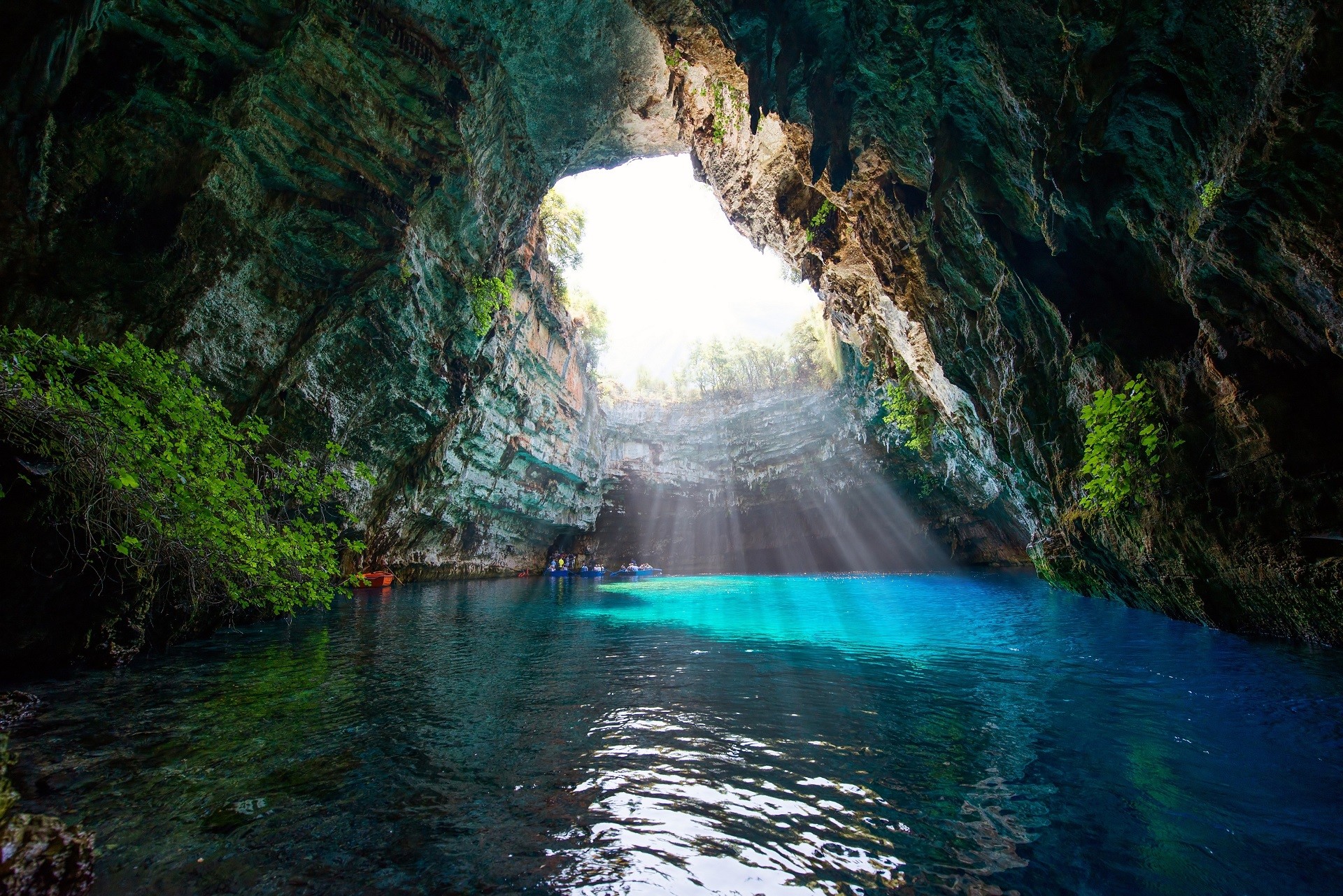 wnętrze jaskini z niebieskim jeziorem i niekompletnym stropem, przez który wpadają promienie słońca