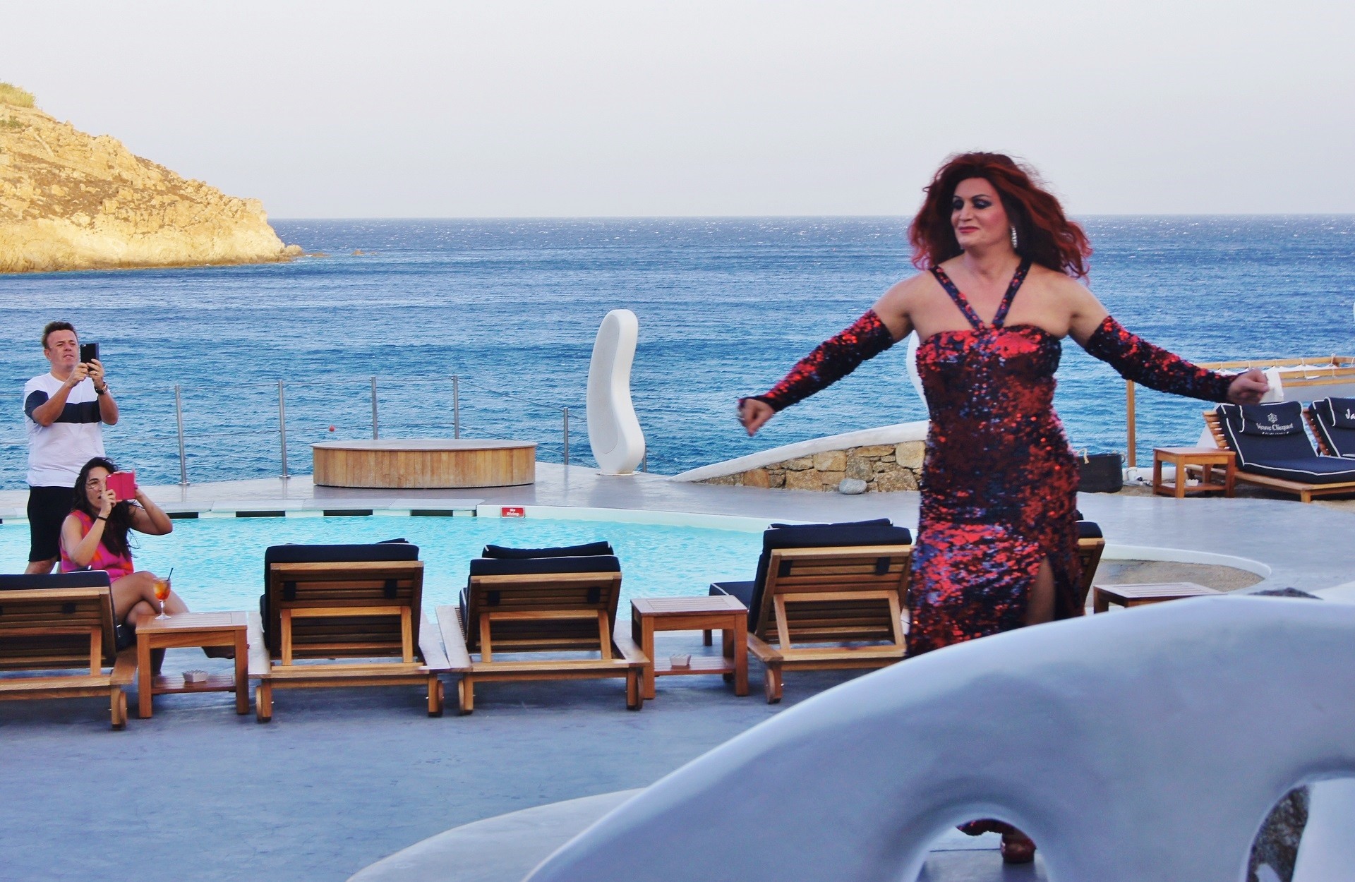 występ drag queen w bordowej cekinowej sukni na tle leżaków, basenu i morza