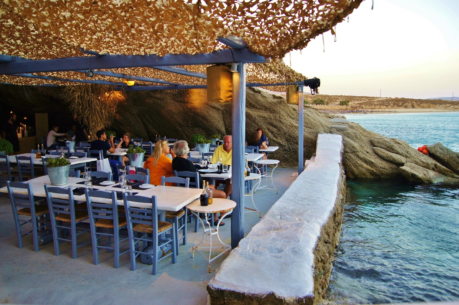 restauracja w jaskini przy morzu ze stolikami, przy których siedzą ludzie