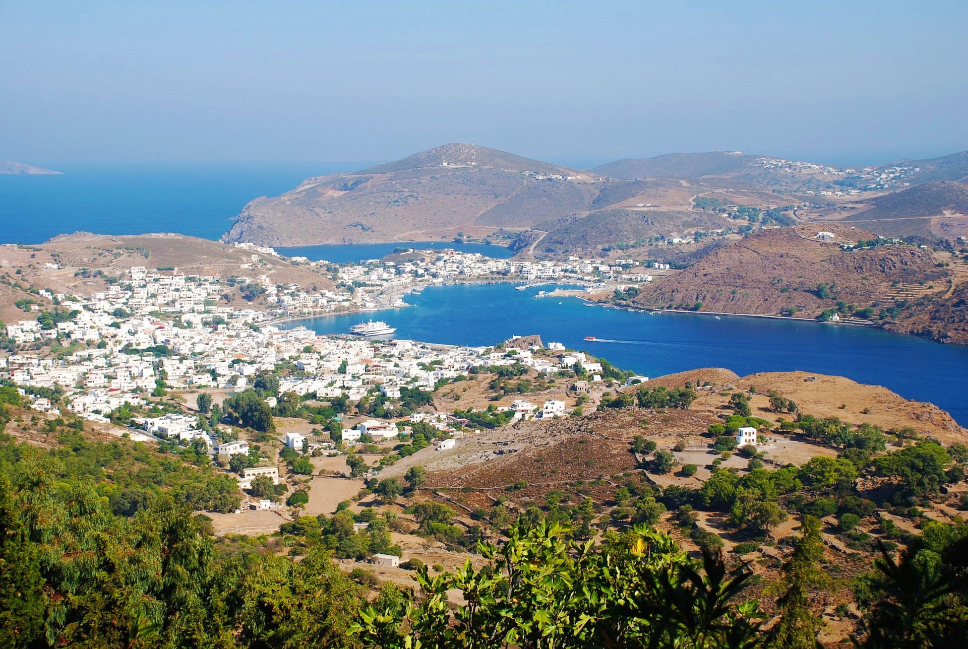 panorama wyspy Patmos z białymi budynkami na brązowych wzgórzach otoczonymi niebieskim morzem