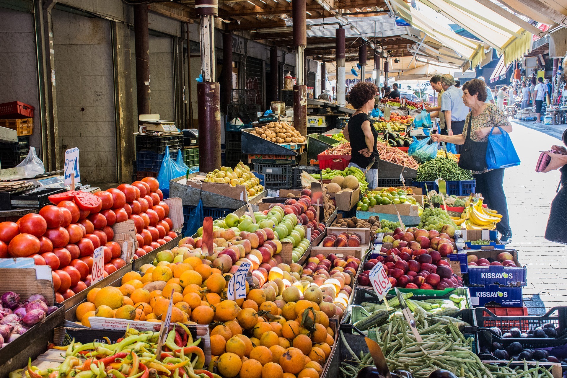 stoiska z warzywami i owocami na bazarze, w tle ludzie robiący zakupy