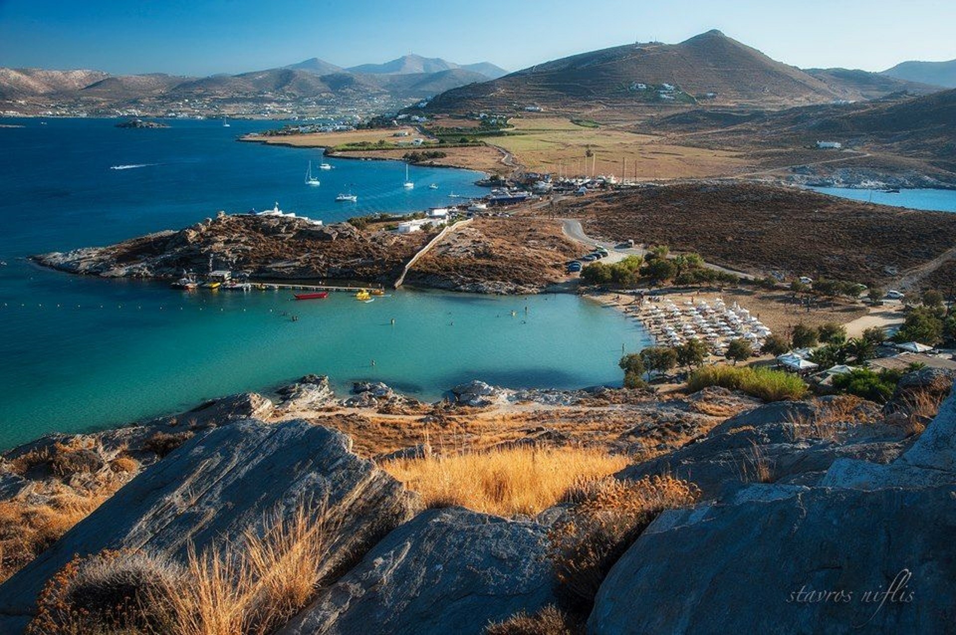 panorama półwyspu oblanego niebieskimi wodami z brązowymi wzniesieniami i plażą z leżakami