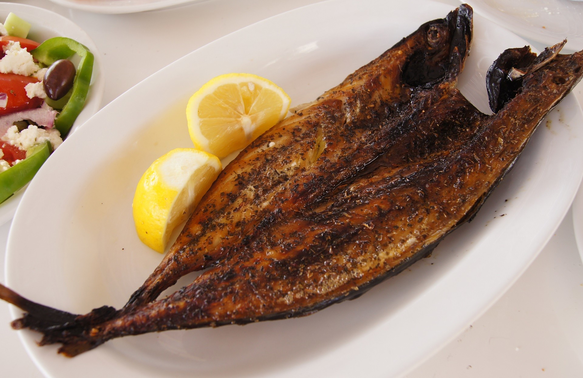 grillowana makrela na białym talerzu obok ćwiartek cytryny