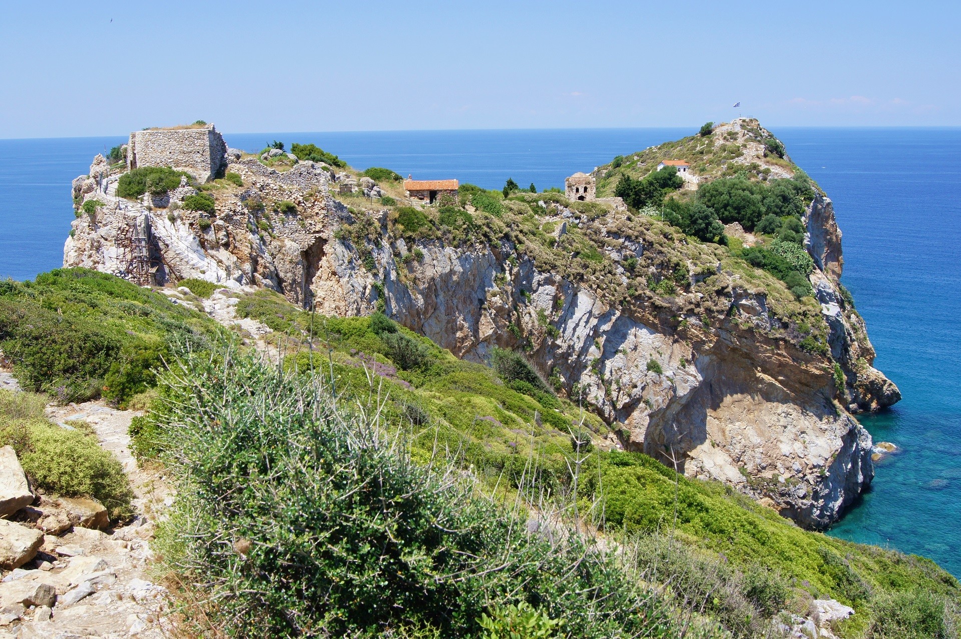 klif porośnięty roślinnością z ruinami bizantyjskiej twierdzy na tle morza i niebieskiego nieba