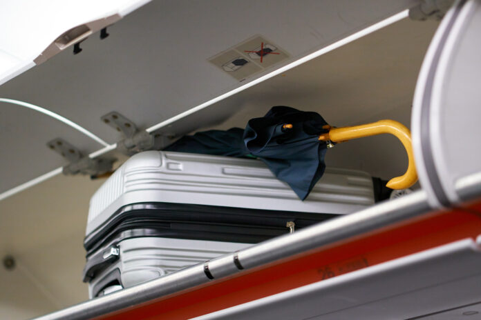 walizka i parasolka w schowku w samolocie