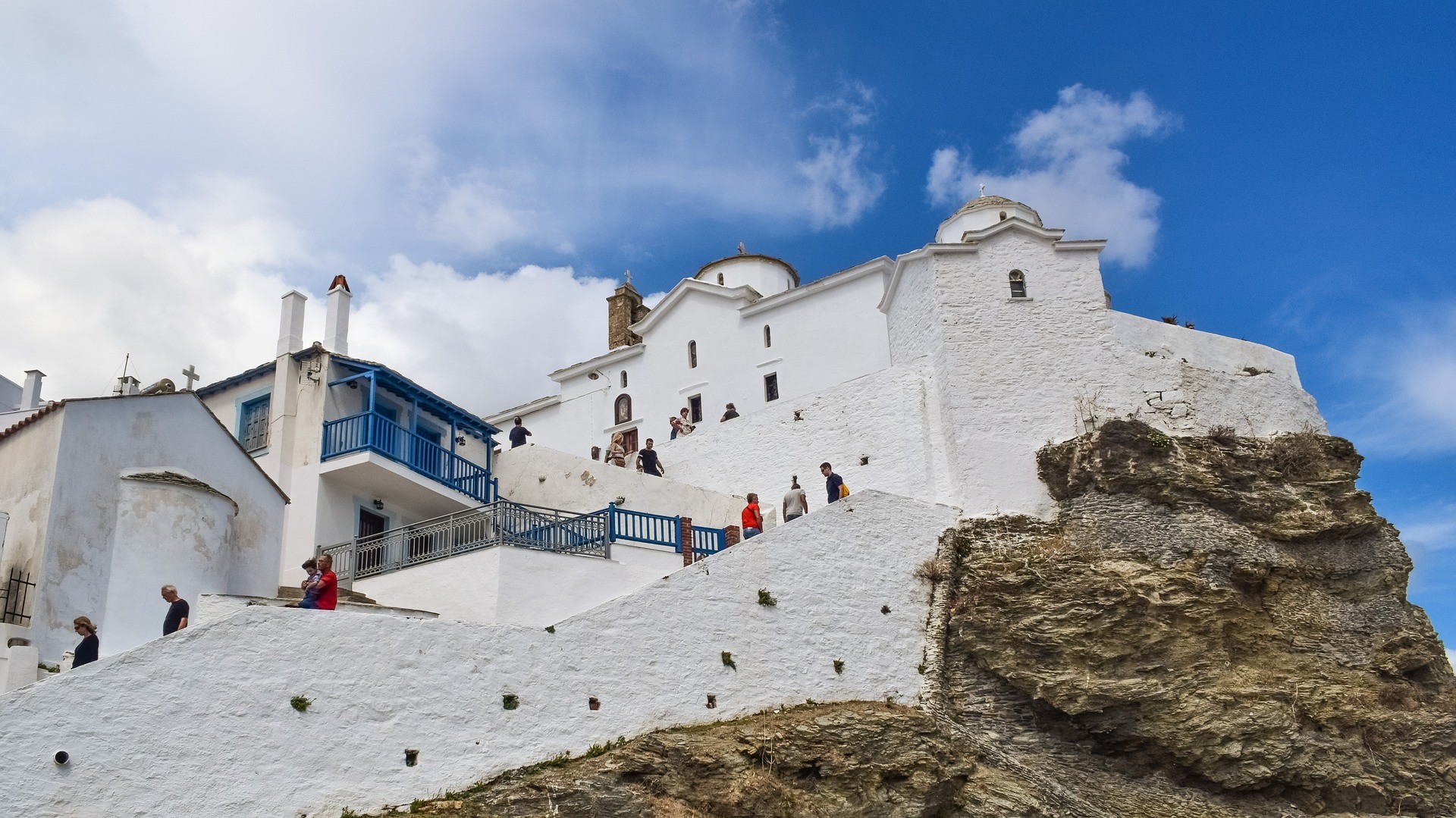 pobielany monastyr wznoszący się na wzgórzu ze schodami, po których schodzą ludzie