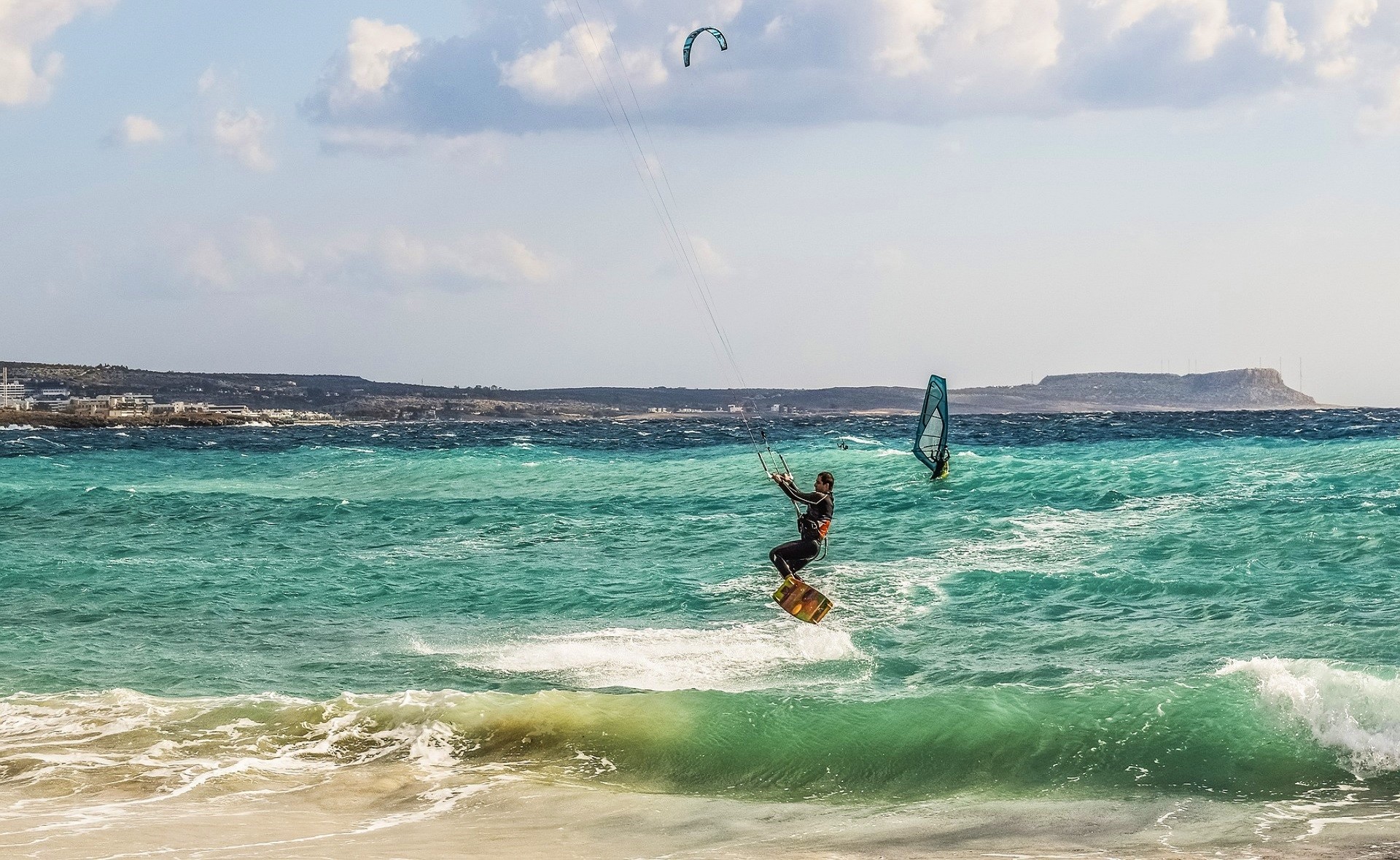 kitesurfer na tle lazurowego morza otoczonego wzniesieniami, w tle windusutfer