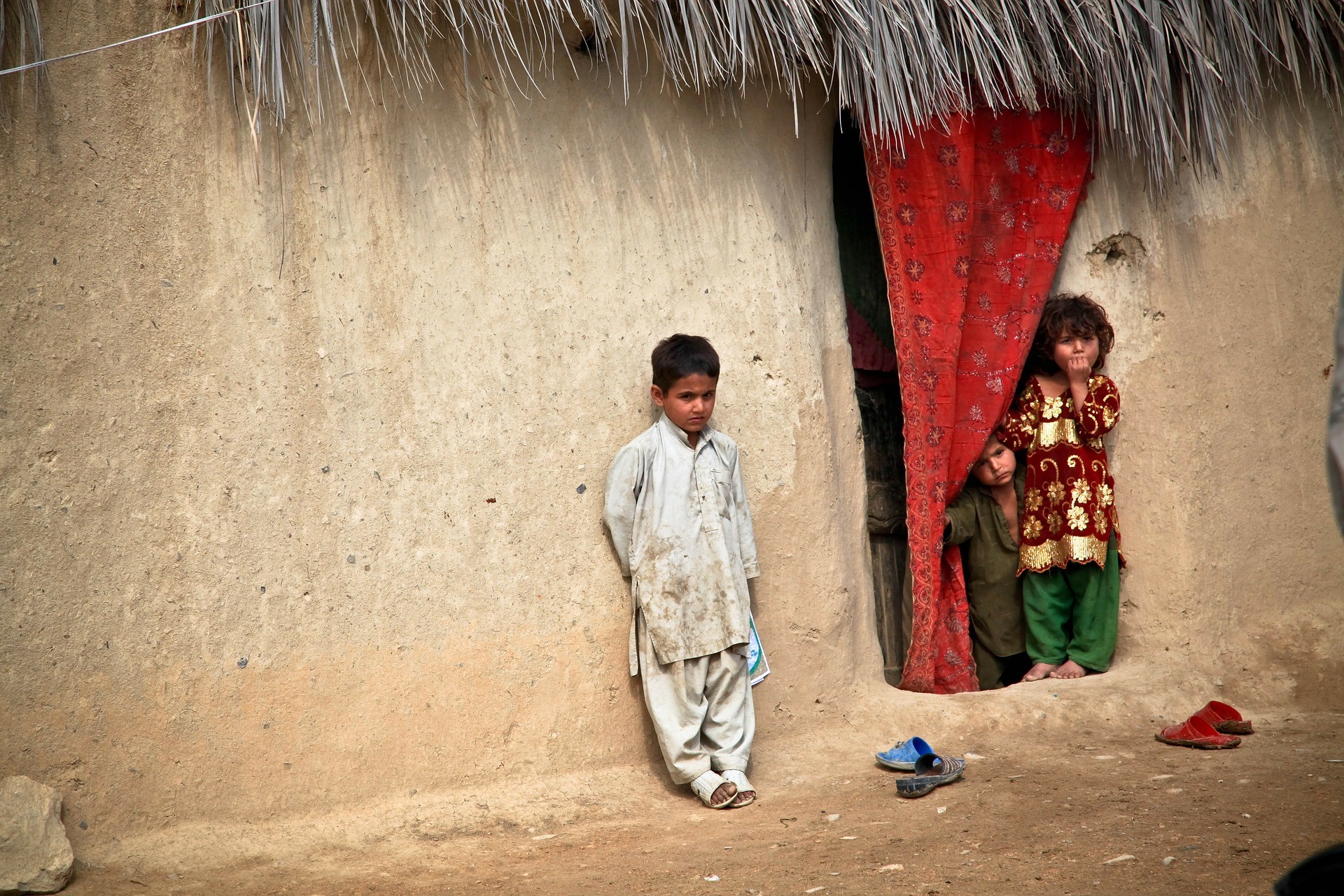 troje dzieci stojących przy botonowym domu w Afganistanie