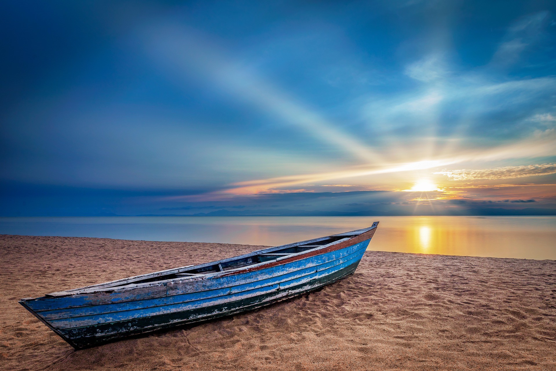 Łódka stojąca na plaży na tle morza i zachodzącego słońca