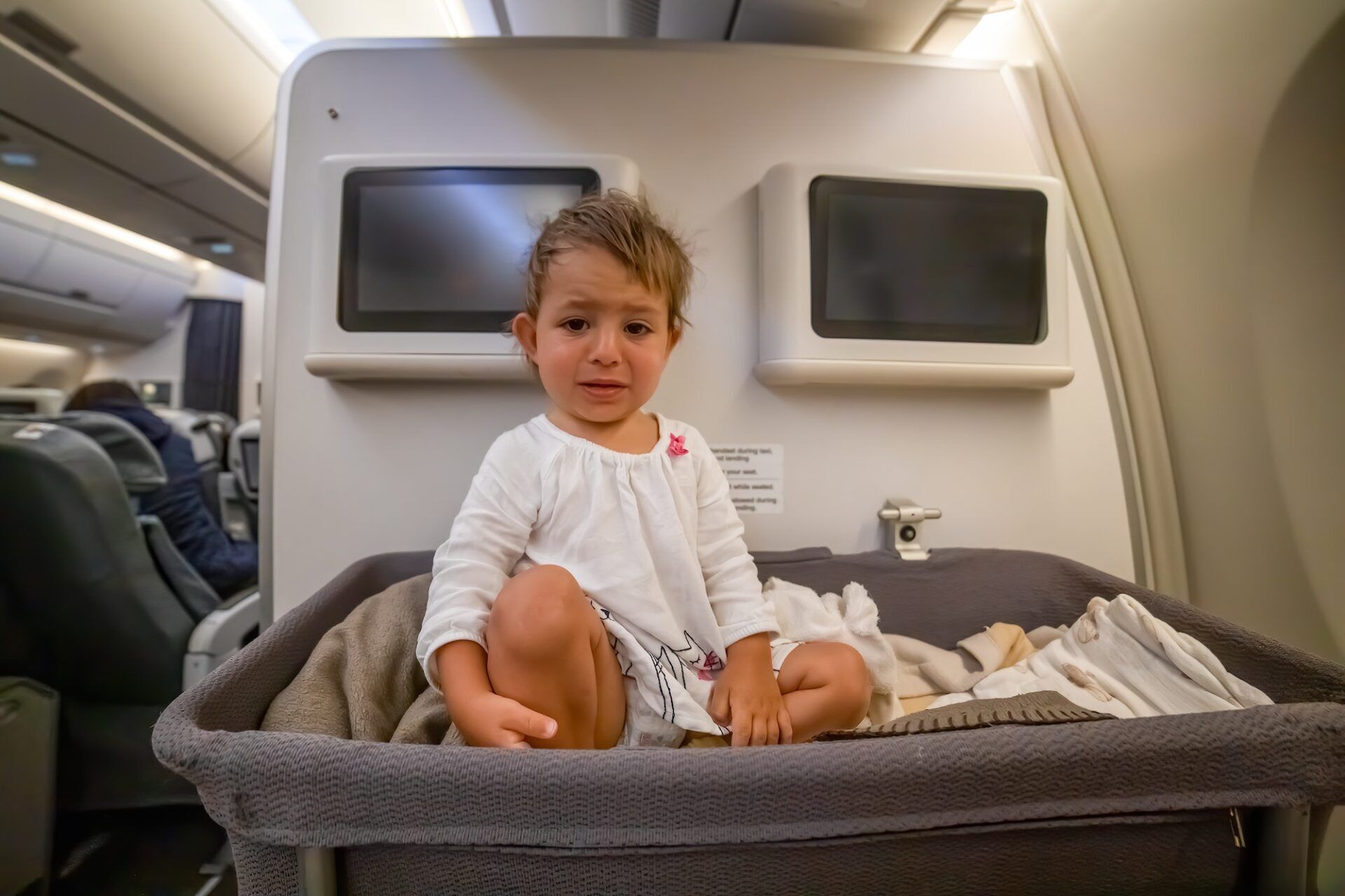 Crying baby in special baby bassinet in airplane. Infant passenger on board