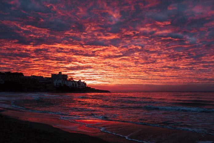 Red sunset at the beach with town in silhouette and dramatic sky with clouds. Amazing sunlight