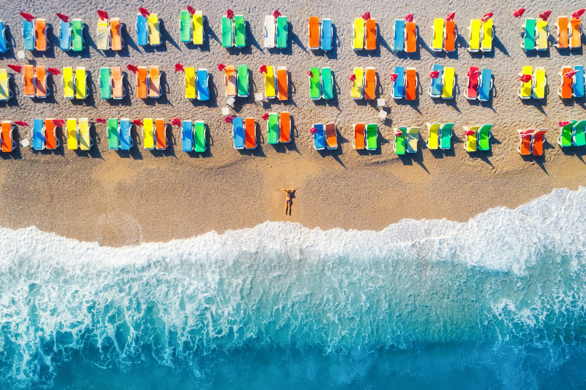 Aerial view of lying woman on the beach with colorful chaise-lounges