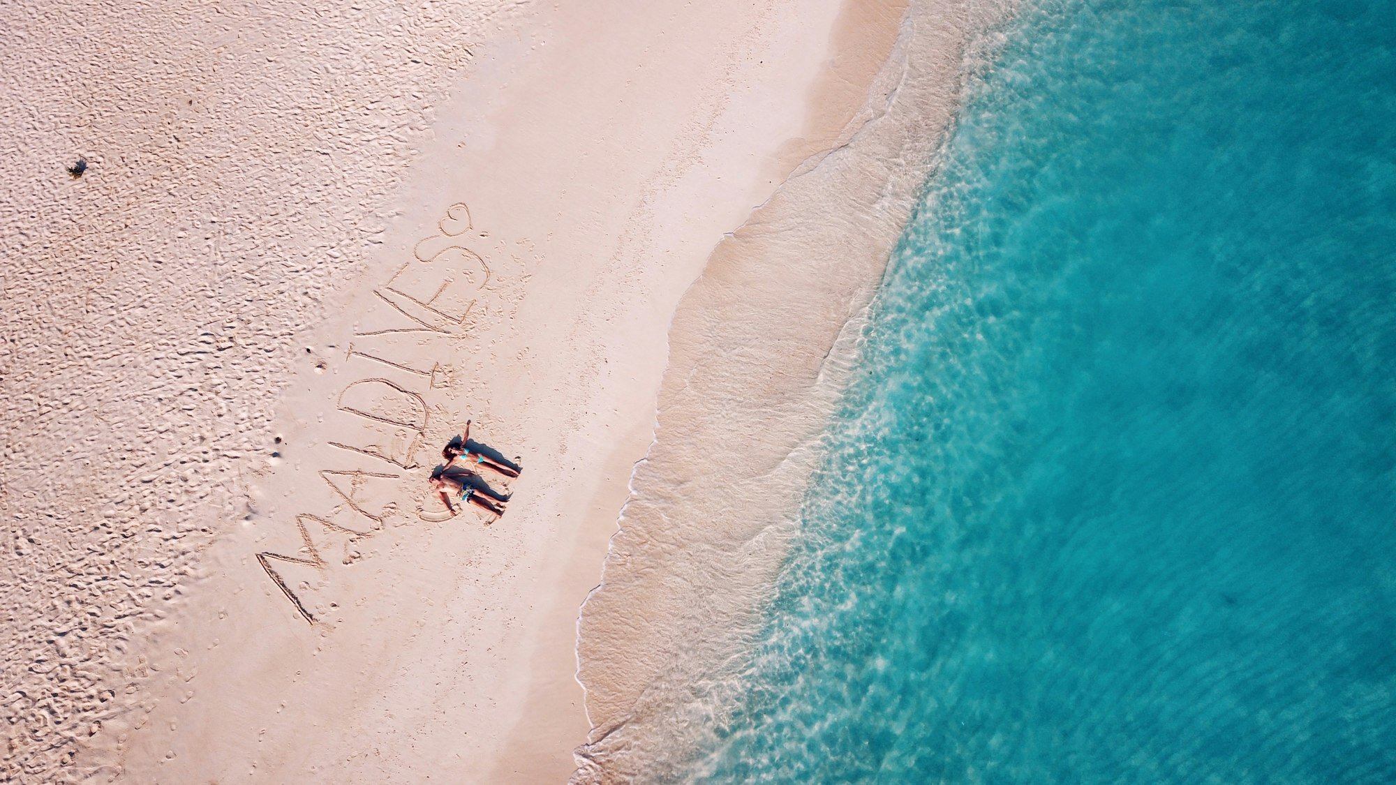 Lovers lie on the sand with the inscription "Maldives"