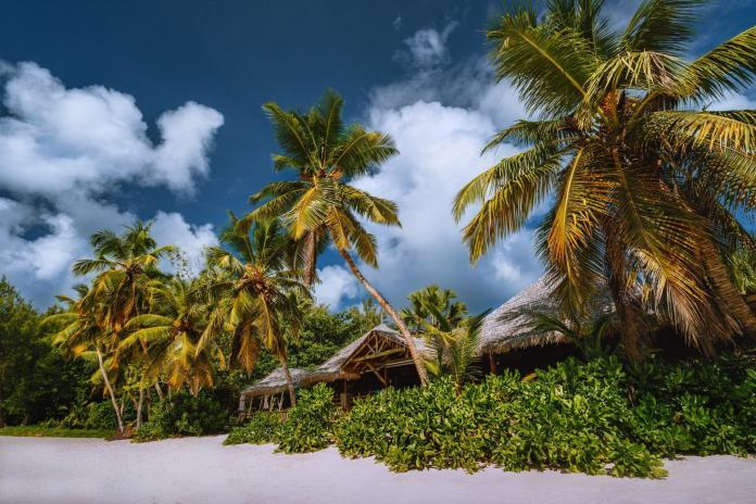 Tropical beach landscape with coconut palm trees and straw roofs. Paradise exotic vacation holidays