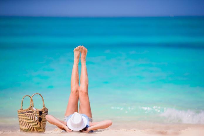 Young beautiful girl relaxing on white beach. Tourist woman enjoy beach vacation lying on the sand