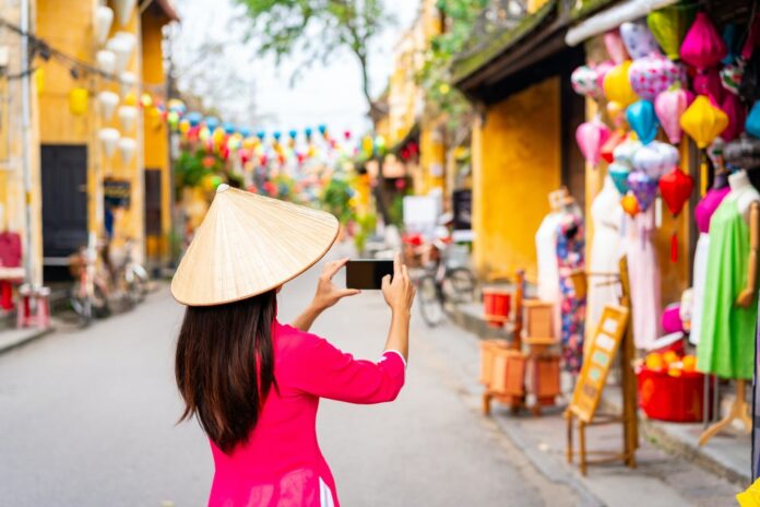 Young female tourist in Vietnamese traditional dress walking at Hoi An Ancient town in Vietnam