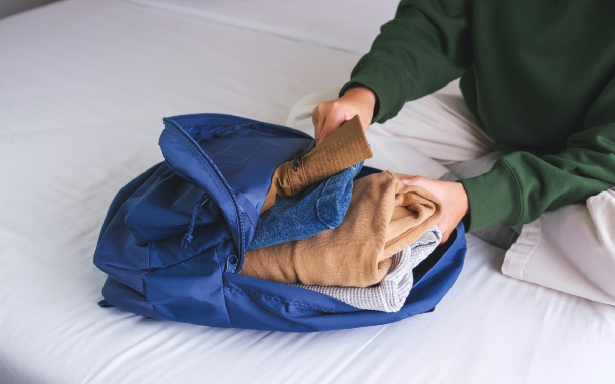 Closeup image of a woman packing clothes in backpack for travel at home