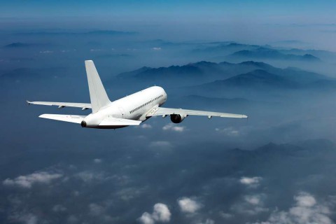 White-passenger-plane-in-the-blue-sky.-Aircraft-flies-high-over-the-clouds-and-foggy-mountain-landscape.-Airplane-view-back-and-top.-shutterstock_539220583
