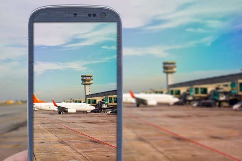 Smatrphone-and-airport-background.-Idea-of-taking-shots-accessing-apps-Internet-blogs-and-others.-The-blur-image-is-an-airport-scene-with-airplane-landed-and-another-taxing-for-taking-off.-shutterstock_2782072