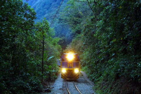 the-train-with-turned-on-head-lights-on-the-inca-track-train-rails-from-hydroelectrica-to-aguas-calientes-machu-picchu-in-peru-with-river-and-mountain-panorama-shutterstock_53595102